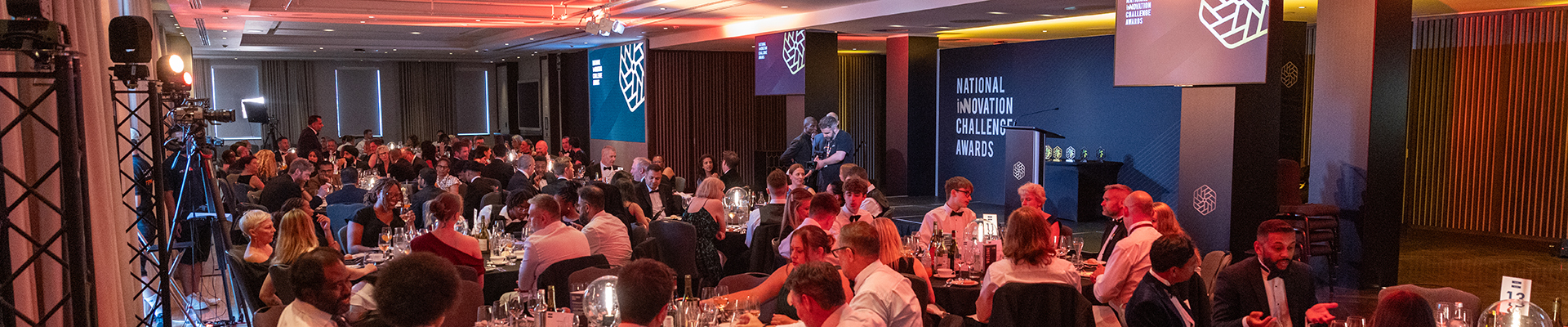 The National Innovation Challenge Awards Cermony - the audience is sitting at tables all dressed in evening wear with the stage behind them with event logos and signage.