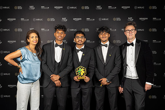 Keith Smith, CEO of HRUC and BBC presenter and STEM ambassador Konnie Huq posing with the colleges category winners (from Uxbridge College) of the National Innovation Challenge 2026. All wearing formal attire standing in front of a wall of logos.