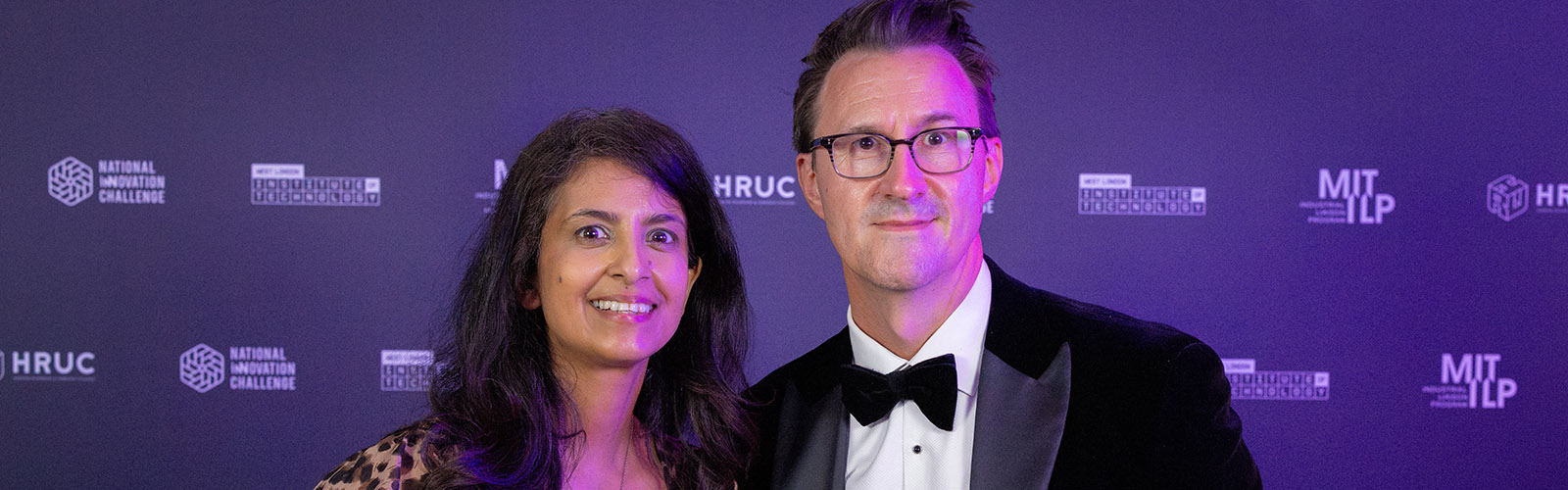 Former Blue Peter TV presenter, and STEM ambassador Konnie Huq with Keith Smith, CEO of HRUC - against a purple backdrop with logos at the NIC awards night.