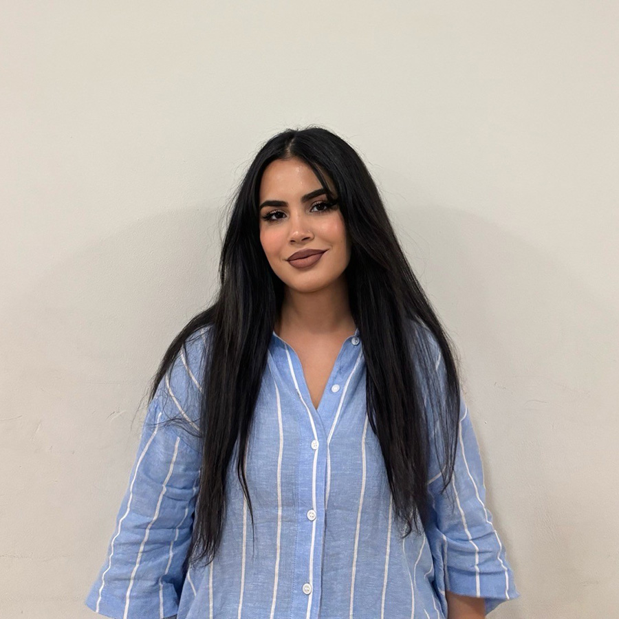 Rukhsar - she has long dark hair and is waring a blue shirt with white stripes 