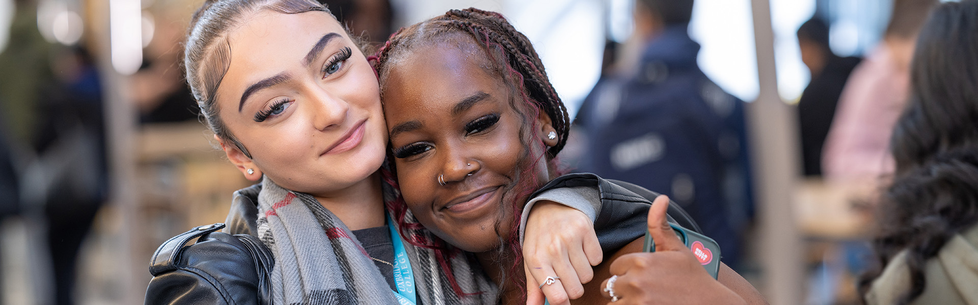 2 x female Uxbridge College students smiling. One is doing a thumbs up. 