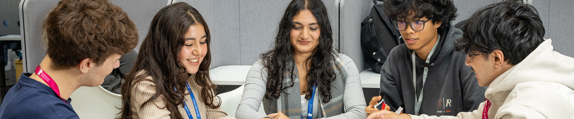 A group of male and female Richmond upon Thames students sitting around a table. They are smiling and playing a game of cards.