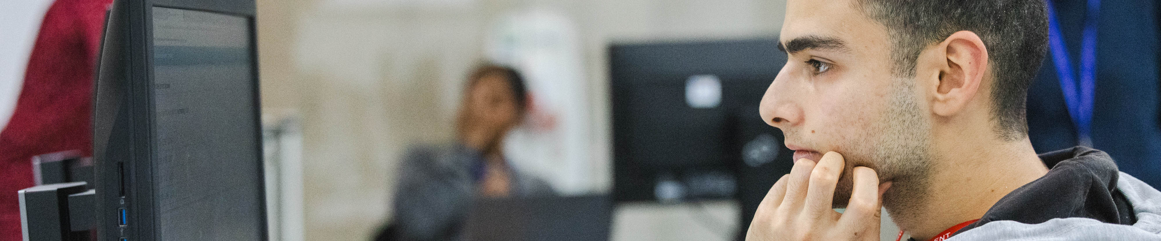 A male student looking at a computer screen with his hand to his face. 
