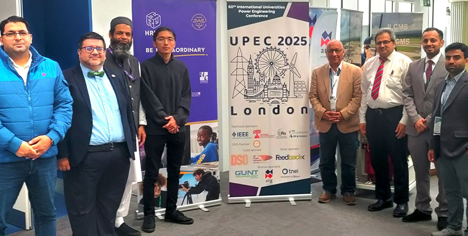 Bektur Ogobaev (wearing glasses and dressed in all black standing in front of the purple banner) posing for a group photo with other members of HRUC, Brunel University and delegates from the Universities Power Engineering Conference (UPEC 2025).