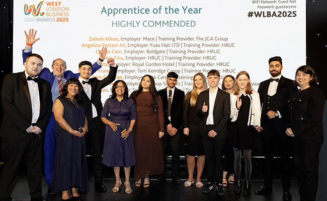 2025 previous highly commended apprentices of the year at the West London Business Awards 2025. The group of winners are all standing in front of a large white screen with thier names on it and are all in evening dress. 