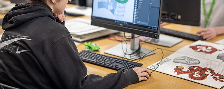 Richmond upon Thames College student at a computer doing course work. Her hand is on the mouse and they are wearing a black hoodie. 