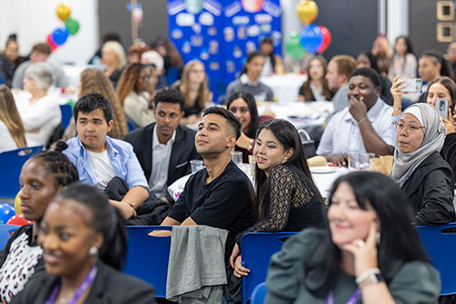 Groups of HRUC students in the audience at the Turing Scheme Overseas Placements ceremony. They are sitting around tables in blue chairs facing towards the speaker.