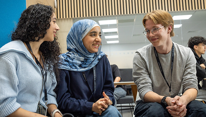Three Richmond upon Thames students sitting and talking together. Two female and one male student who is wearing glasses and smiling.