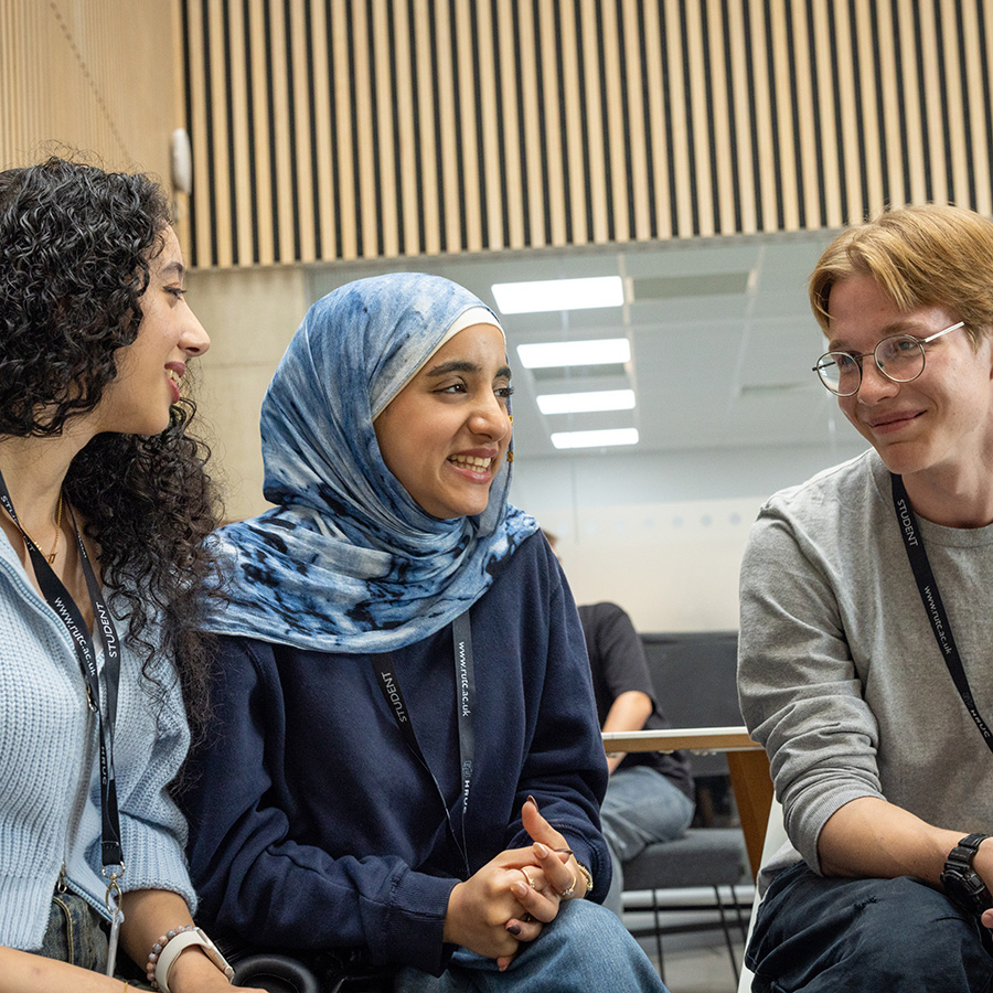Three Richmond upon Thames students sitting and talking together. Two female and one male student who is wearing glasses and smiling.