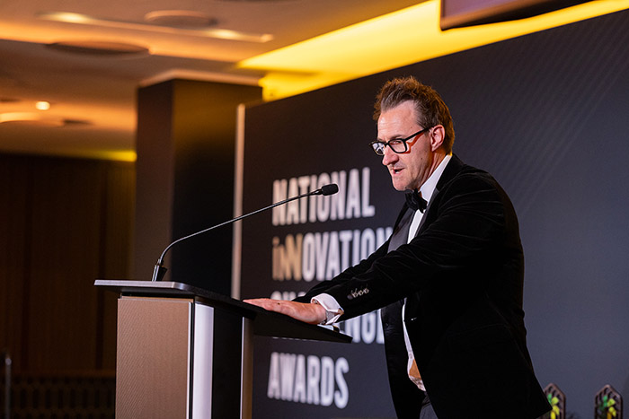 Keith Smith, CEO of HRUC standing on stage at the National Innovation Challenge awards ceremony, speaking at a lectern.