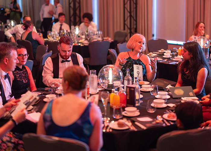 People dressed in formal wear at the National Innovation Competition Awards Ceremony, sitting around a table and talking to each other.