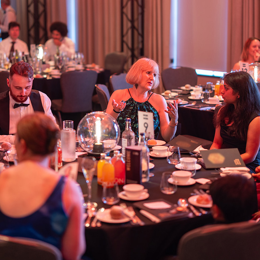 People dressed in formal wear at the National Innovation Competition Awards Ceremony, sitting around a table and talking to each other.