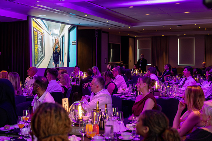 Staff, students and guests at the National Innovation Challenge awards ceremony 2026 watching one of the finalists videos on screen. Everyone is dressed in formal wear and sitting at tables.