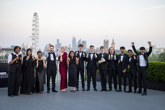 All the finalists of the National Innovation Challenge on the roof terrace of the IET. Dressed in formal wear and giving a thumbs up with a London skyline behind them.