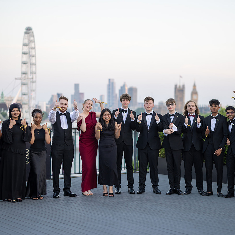 The group of finalists for the 2026 National Innovation Challenge standing on the IET terrace with the London skyline behind them, giving a thumbs up. They are all wearing formal attire.