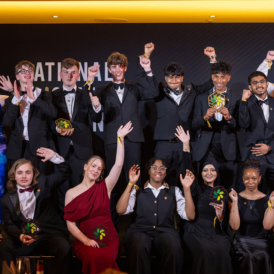 Our 2026 National Innovation Challenge winners and finalists with BBC presenter and STEM ambassador Konnie Huq on stage at the awards ceremony. Everyone is dressed in formal wear, holding their trophies with arms in the air. 