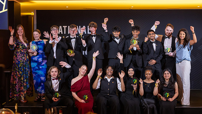 Our 2026 National Innovation Challenge winners and finalists with BBC presenter and STEM ambassador Konnie Huq on stage at the awards ceremony. Everyone is dressed in formal wear, holding their trophies with arms in the air.
