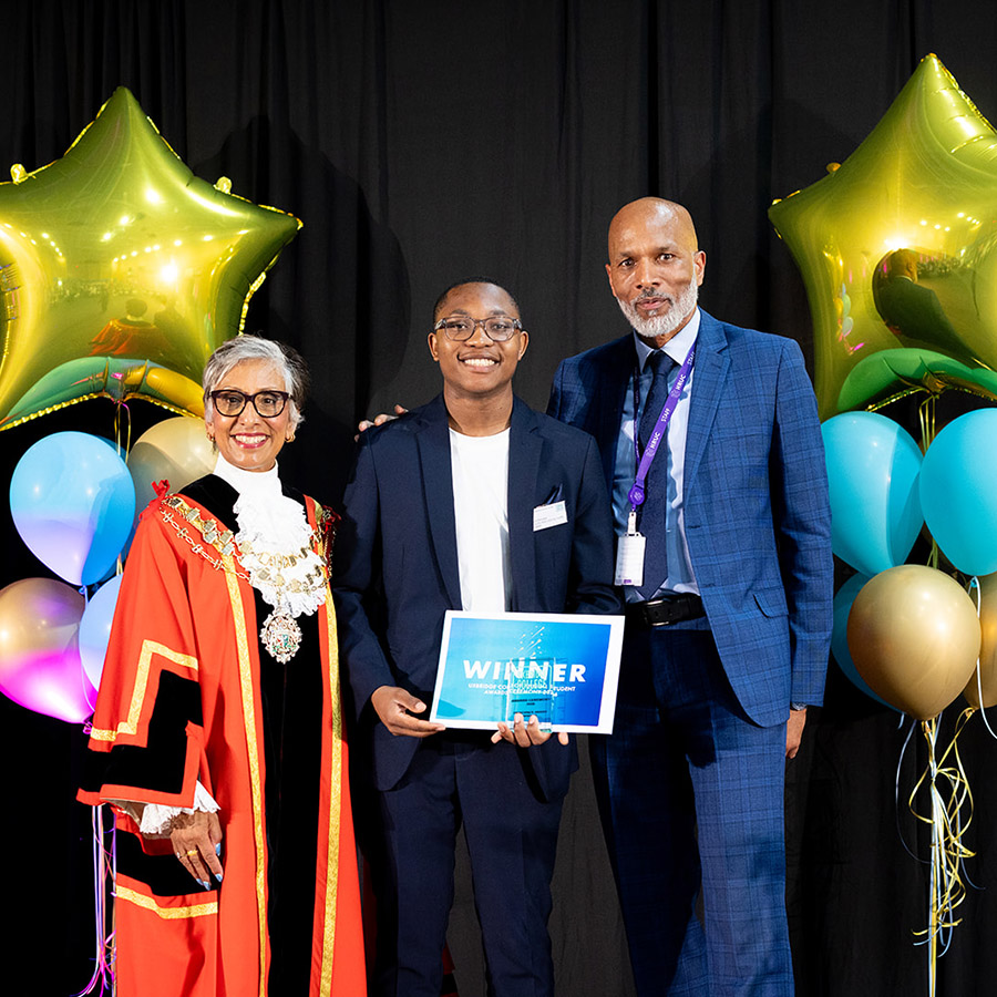 Clive Hodge, Principal of Uxbridge College, The Worshipful Mayor of the London Borough of Hillingdon, Councillor Reeta Chamdal and Level 3 Health and Social Care student Nigel Nkomo holding his Principal’s Award. Balloons and gold star balloons are at the back of them. The Mayor is wearing her ceremonial robes. 
