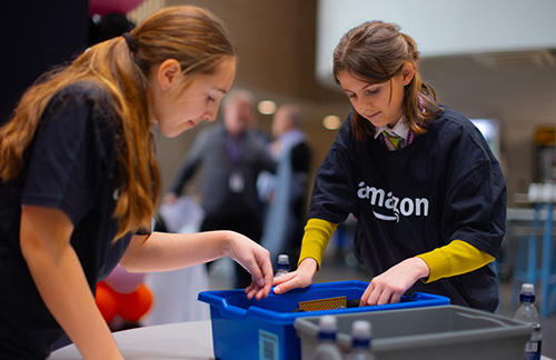 Two girls engaging in the interactive sessions at Amazon’s Flagship Girls' Tech Day Event at Richmond upon Thames College. They are both wearing navy blue Amazon t-shirts.