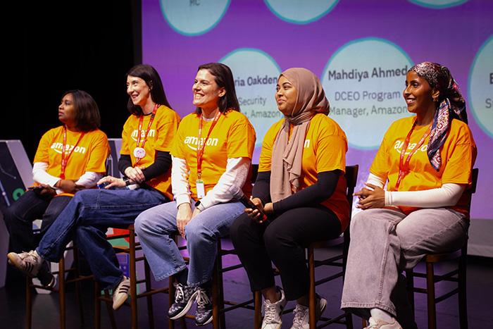 A panel discussion with a diverse group of female Amazon leaders on the Amazon’s Flagship Girls' Tech Day Event. All dressed in orange Amazon t-shirts. 