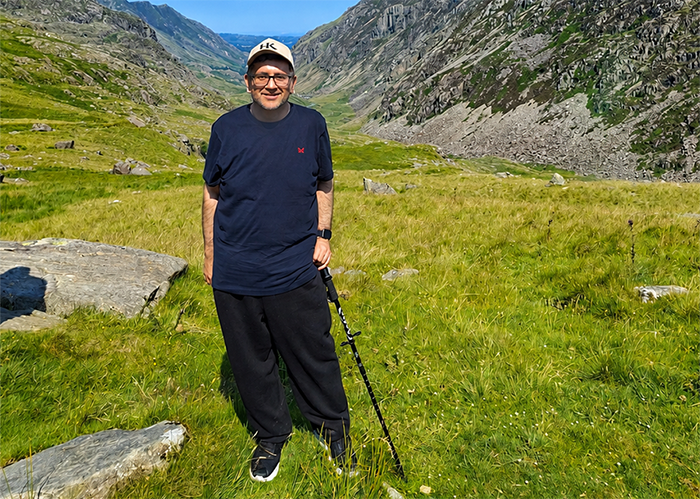 Asif Khan - Assistant Principal for Engineering, Technologies, Higher Education - on his epic walking challenge. He has green grass, rocks and mountains around him with clear blue skies. 