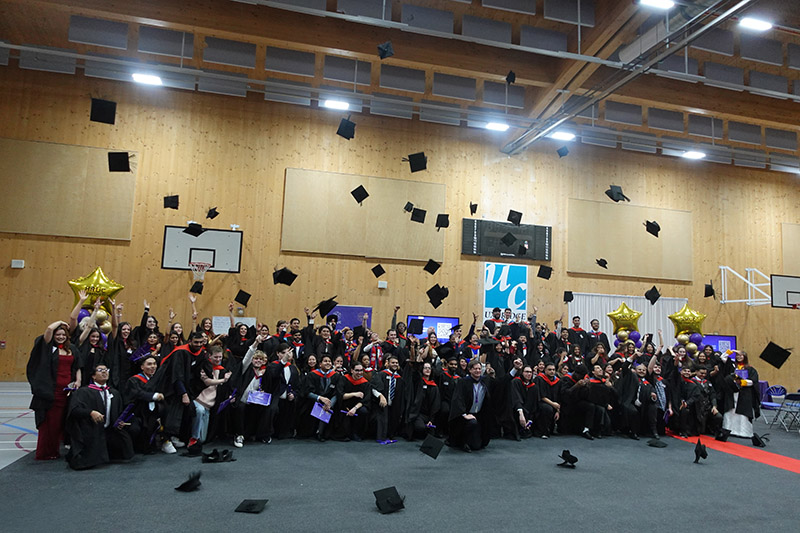 HRUC HE graduates throwing their black caps in the air. 