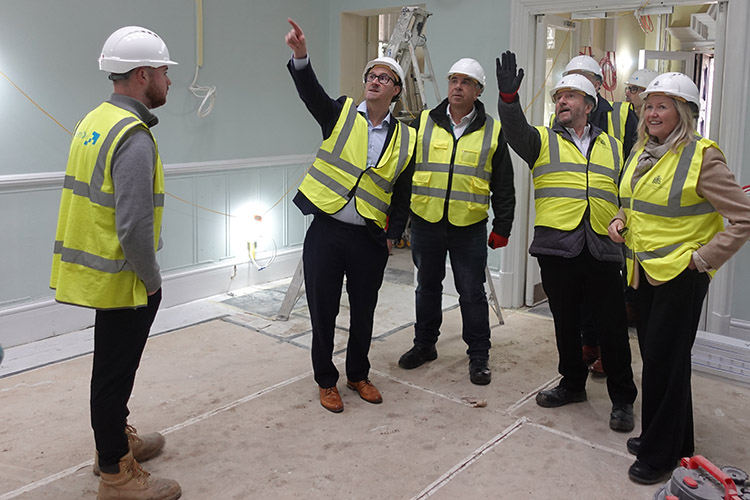 Keith Smith with others at Barra Hall. They are pointing to the building work that is ongoing and all wearing yellow high-visibility vests and white safety helmets.