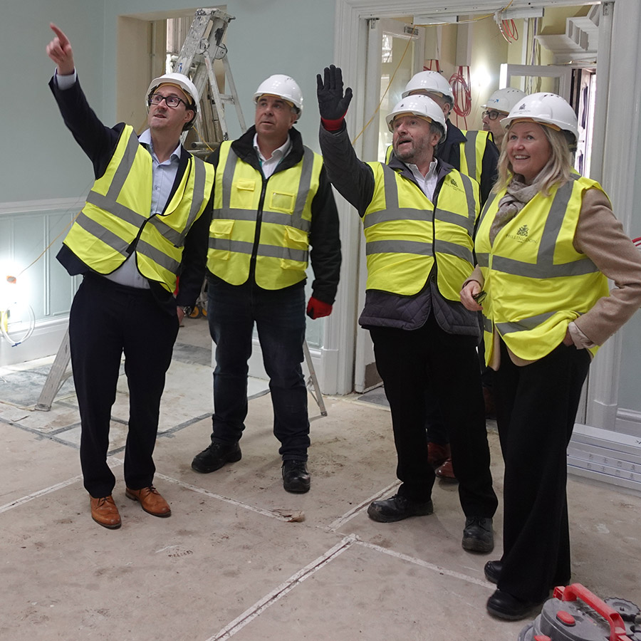 Keith Smith with others at Barra Hall. They are pointing to the building work that is ongoing and all wearing yellow high-visibility vests and white safety helmets.