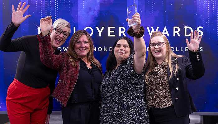 Four female employers holding up their award at the HRUC Employer Awards at Uxbridge College. They are holding a hand in the air and smiling big.
