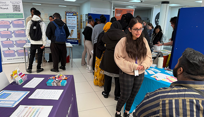 Students gathered at the HRUC Mental Health Fair. There are tables with leaflets layed across them and stand up banners with further information.