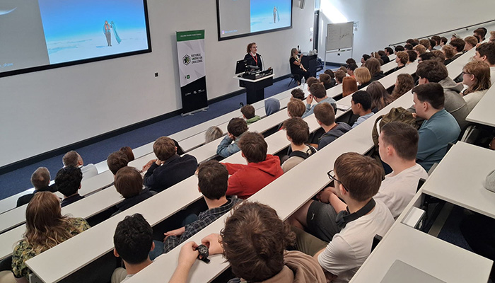 Dr Niamh Shaw giving a lecture at Exeter College. Students are sitting in a lecture theatre looking at a screen with images of Dr Shaw in Antarctica.