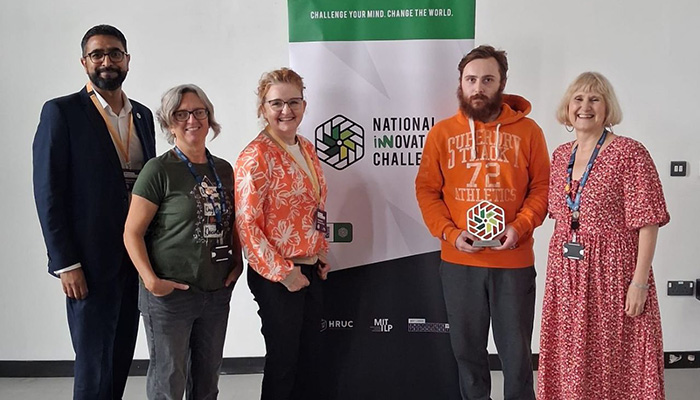 Yaseen Akhtar, Managing Director of the West London Institute of Technology, and Dr Niamh Shaw, NIC ambassador with staff and our NIC 2026 finalist from Ysgol Gyfun Gymraeg Bro Edern in Wales. They are standing next to a NIC pull up banner and the student is holding his trophy.