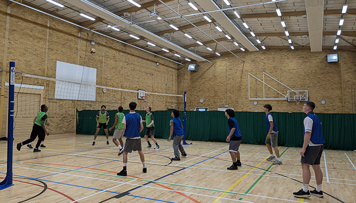 HRUC students playing volleyball in a sports hall. They are wearing green and blue bibs.