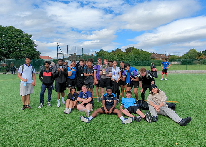 Our students gathered together on a sports field for the HRUC Sports Day - posing for a group photo. They are all dressed in sports gear and one female student is holding a cup in the middle of the group.