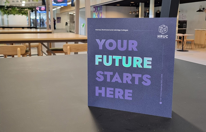 The prospectus booklet is sitting on a table with Uxbridge mall and cafe behind it. The cover is purple and says: Your Future Starts Here
