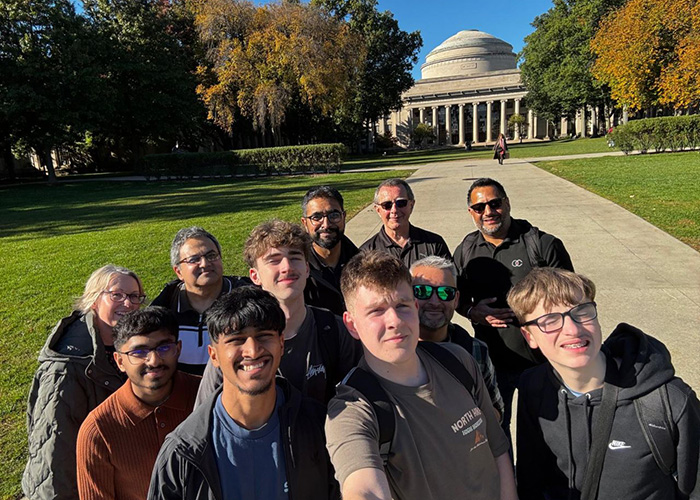 The winners of the National Innovation Challenge (NIC) 2026  with chaperones and Yaseen Akhtar, Managing Director of the West London Institute of Technology in the US. They are gathered togehter to take a selfie in front of a green lawn with a large domed building behind them at MIT, Boston. 