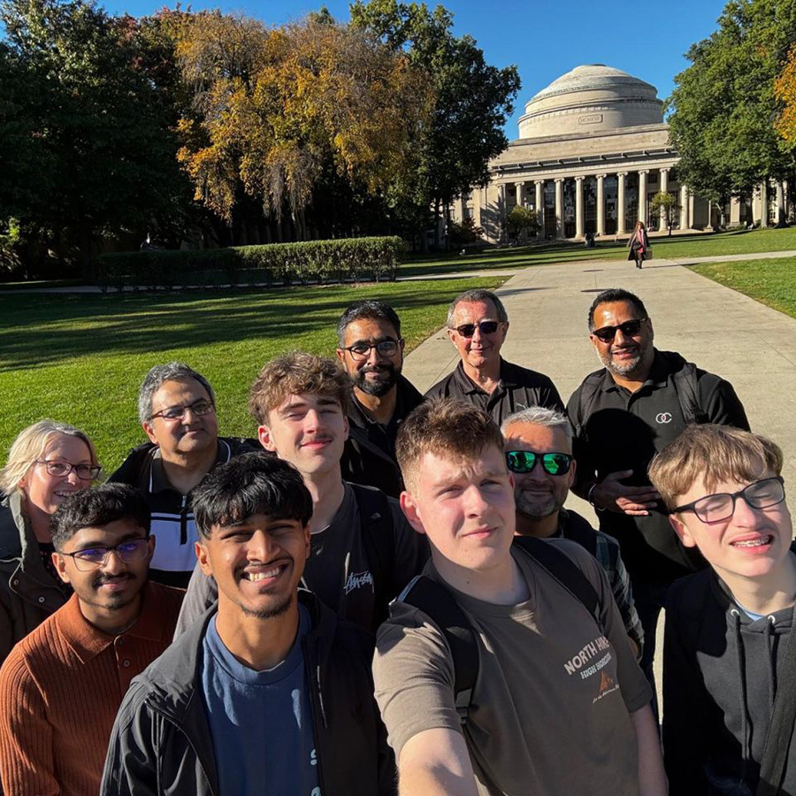 The winners of the National Innovation Challenge (NIC) 2026  with chaperones and Yaseen Akhtar, Managing Director of the West London Institute of Technology in the US. They are gathered togehter to take a selfie in front of a green lawn with a large domed building behind them at MIT, Boston. 