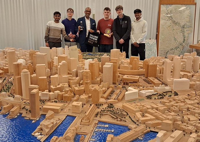 Our 2026 NIC winers standing in front of a large model of a city. They are also holding NIC merchandise - water bottle and tote bag as well as the gold trophy.