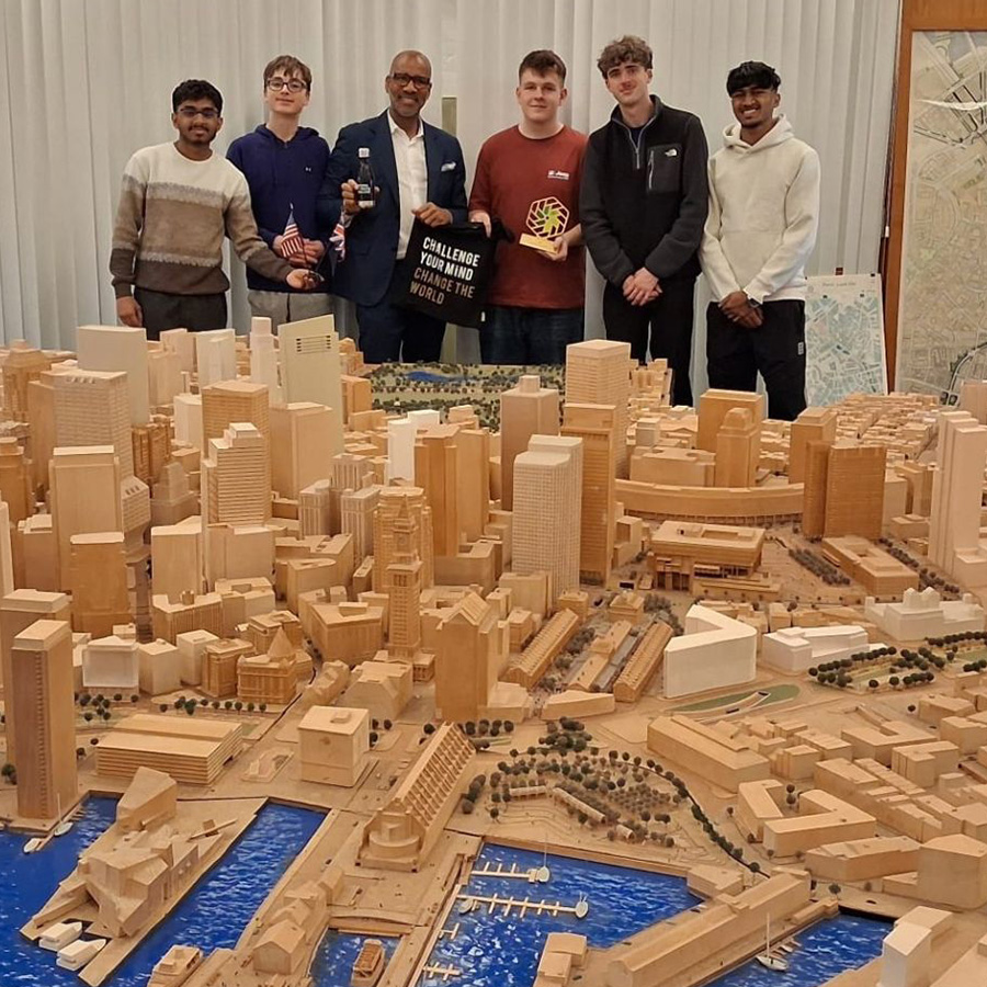Our 2026 NIC winers standing in front of a large model of a city. They are also holding NIC merchandise - water bottle and tote bag as well as the gold trophy.