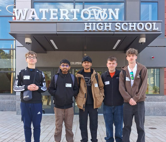 Our NIC 2026 winners standing in front of Watertown High School. There is a building behind them with the name of the school on it.