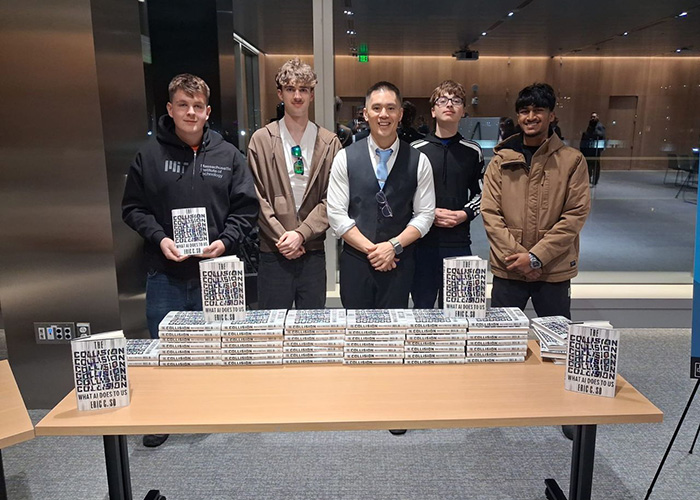 Our NIC 2026 winners standing with Professor Eric So behind a table of his books, in front of large windows. His book is called 'The Collision: What AI Does to Us'.