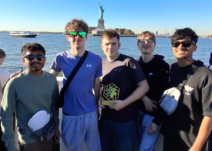 Our NIC 2026 winners on a boat with the Statue of Liberty behind them. They are holding a gold NIC trophy.