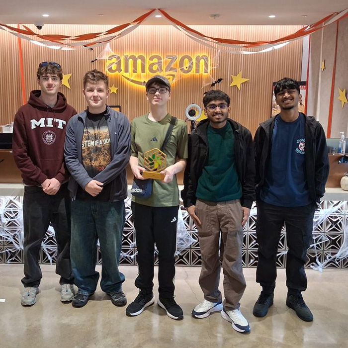 Our NIC 2026 winners standing in front of Amazon reception area with the Amazon sign behind them in yellow and Halloween decorations are displayed. They are holding the NIC gold trophy.