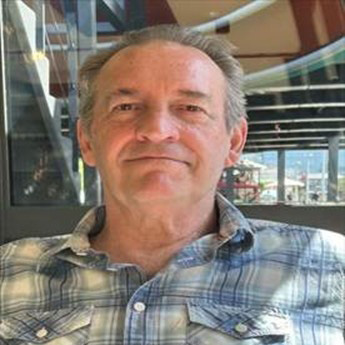 Ian Collier, grinning at camera, wearing a blue and cream checked shirt