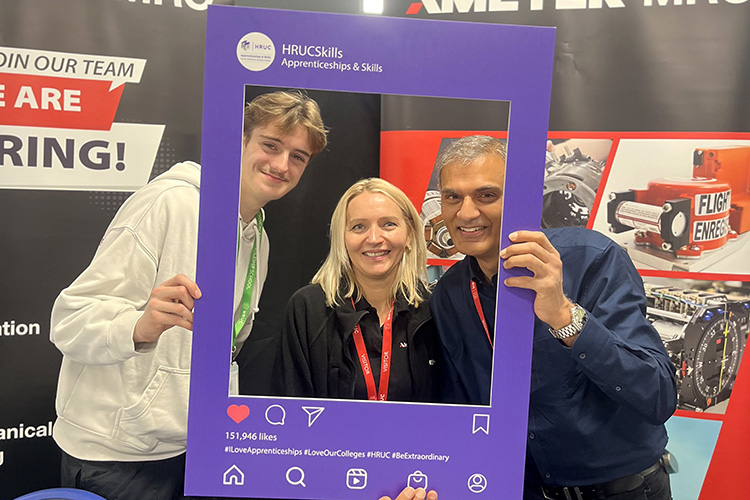 HRUC staff and student at the Apprenticeship Careers Fair. They are holding up an HRUC Apprenticeship and Skills branded frame and smiling through it.