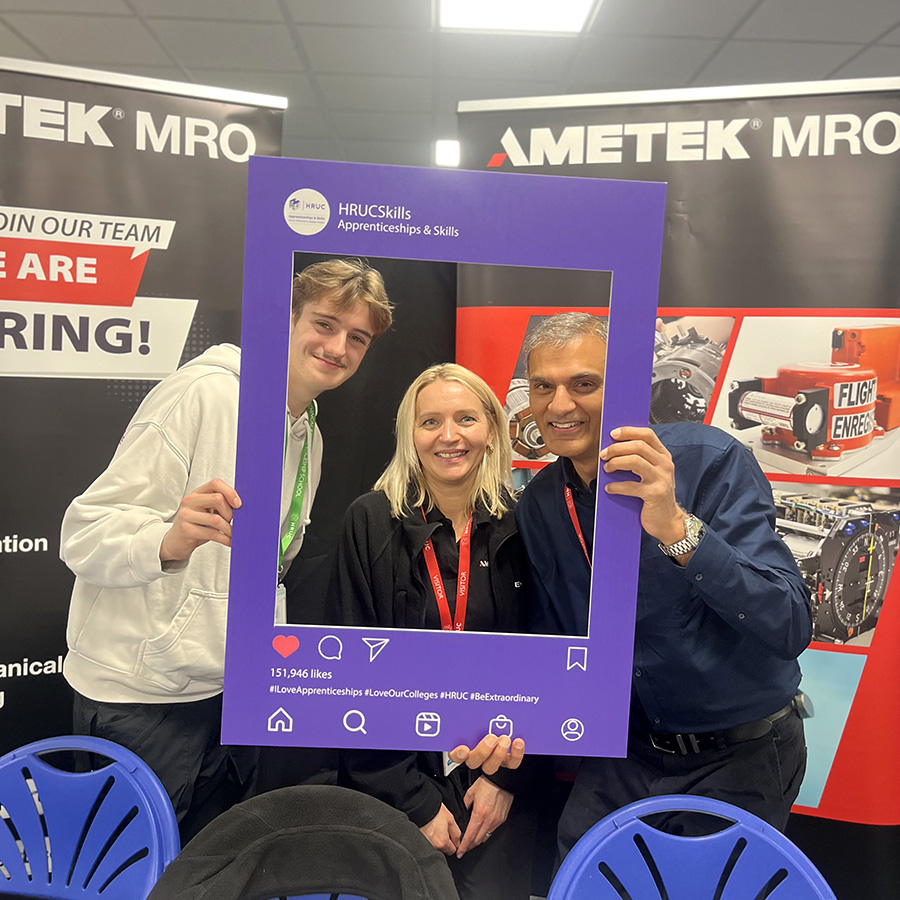 HRUC staff and student at the Apprenticeship Careers Fair. They are holding up an HRUC Apprenticeship and Skills branded frame and smiling through it.