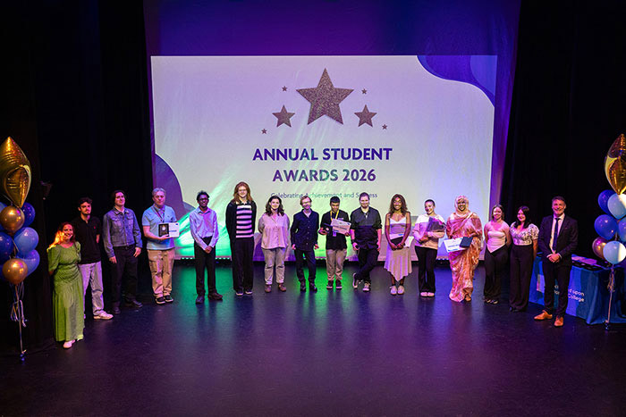 Richmond upon Thames College Student Award winners standing on stage, holding their awards with a screen behind them that says: Annual Student Awards 2026. There are balloons either side of them.
